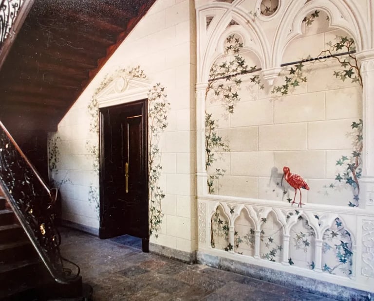 Hallway with wooden staircase and large mural of faux sandstone, ivy, gothic arches, and red bird.