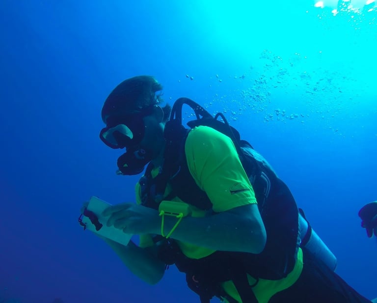 A scuba diver in yellow gear writes on an underwater slate while diving in deep blue ocean water.