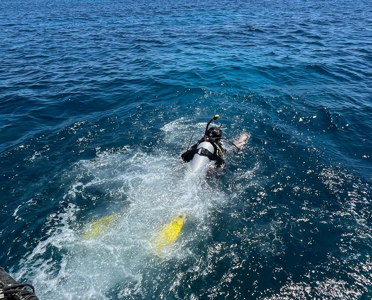 A scuba diver with yellow fins jumps into the deep blue ocean water from a boat during a diving excursion.