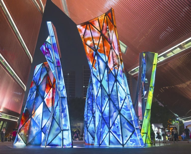Blooming Sculpture lit up at night with its multi-colored glass panels and people walking around it