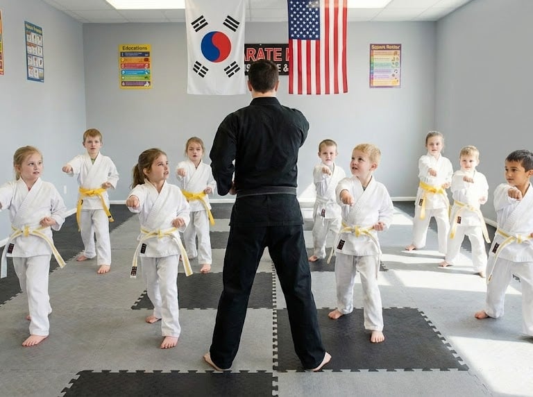 Young children in white uniforms practice punches in a martial arts class with a black belt karate instructor.