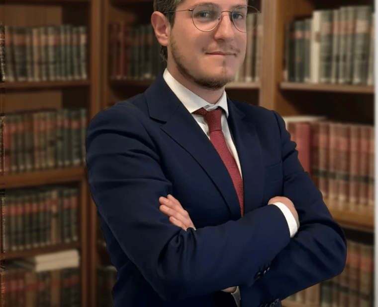 Professional male lawyer in a navy blue suit standing in a legal library with books.