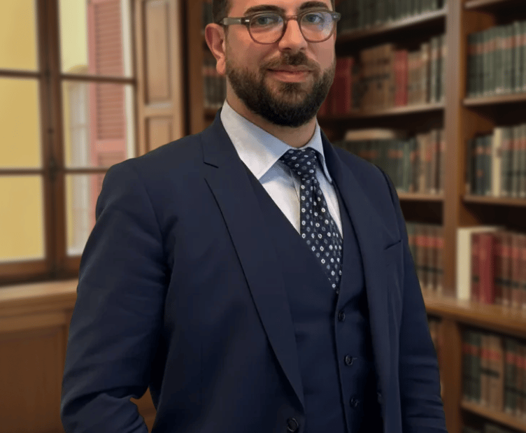 Lawyer in a navy blue three-piece suit standing in a classic library with bookshelves.