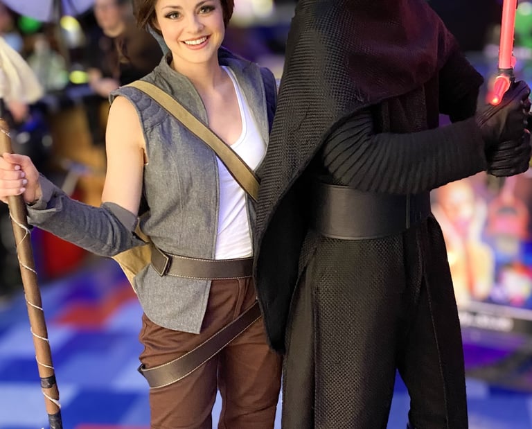 Star Wars fans in Rey and Kylo Ren cosplay posing with a lightsaber and staff at a convention.
