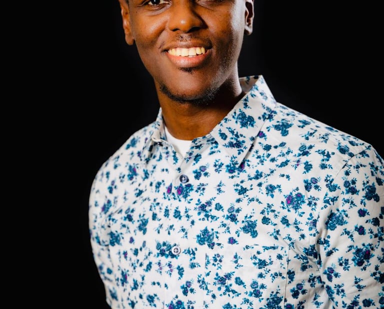 Portrait of a smiling young Black man in a stylish white and blue floral short-sleeved shirt.