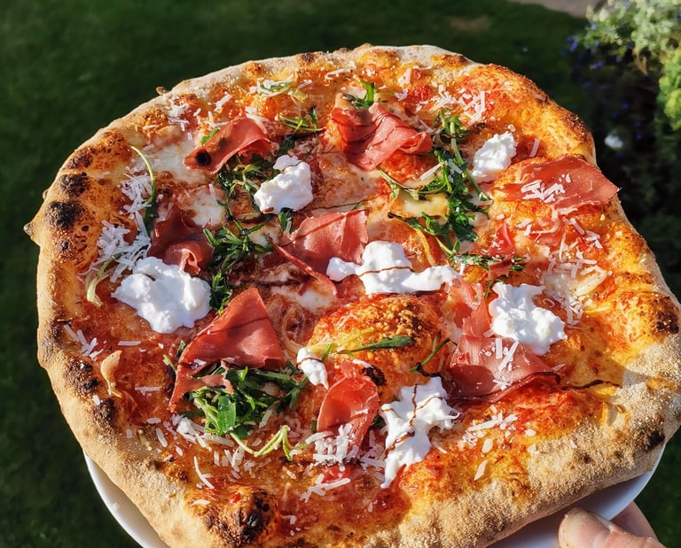 Handmade Neapolitan pizza with prosciutto, burrata cheese, and arugula over a crispy sourdough crust.