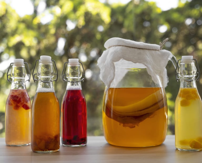 Kombucha casera en un frasco de fermentación con SCOBY y botellas saborizadas de bebida probiótica.