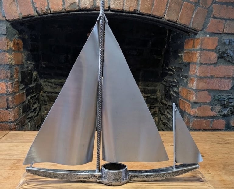 A large sailboat sculpture made from recycled metal materials sitting on a scorched wood stand