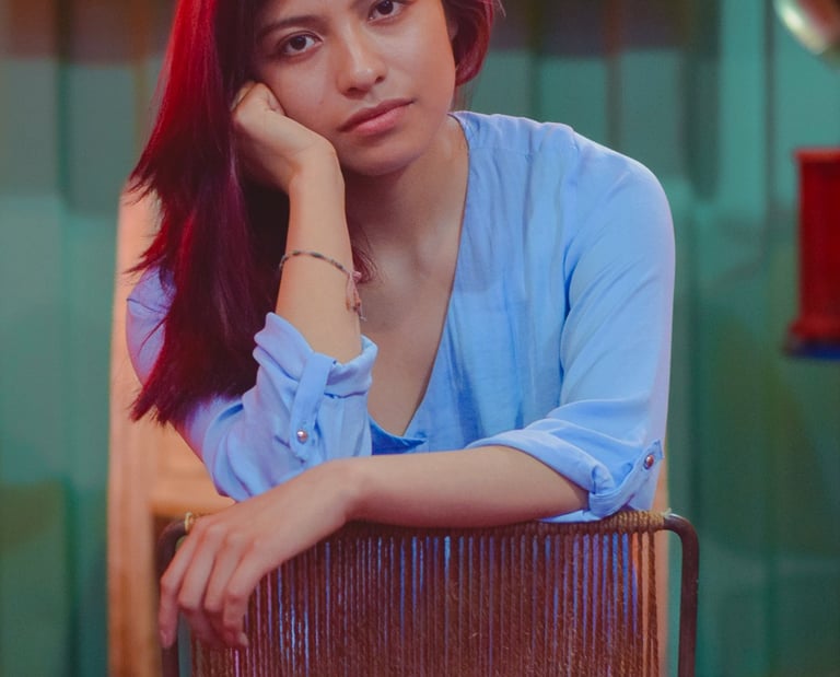 A young woman with auburn hair in a blue blouse sits on a vintage chair.