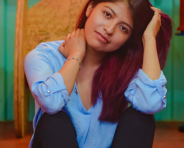 Young woman with auburn hair in a blue shirt sitting on the floor in a studio setting.