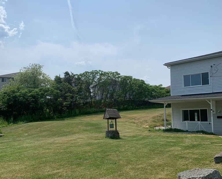 A white suburban house with a rustic wishing well on a freshly cut lawn under a bright blue sky.