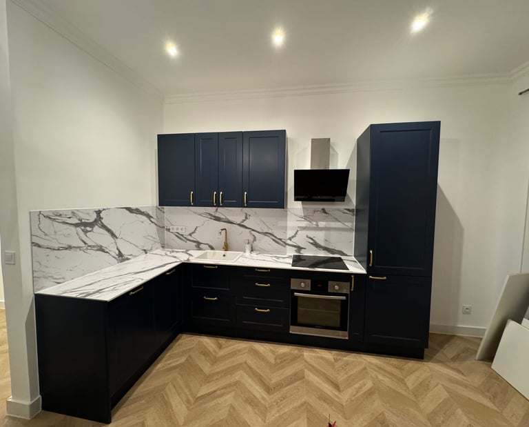 Réalisation d'une cuisine équipée avec plan de travail en marbre, meubles noirs et parquet chevron. Harenova