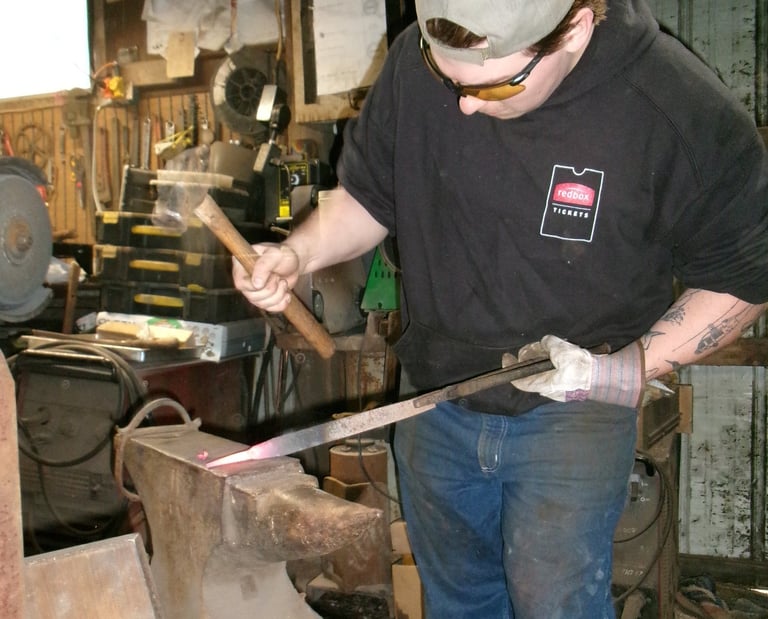 A blacksmith in a workshop uses a hammer to shape glowing hot metal on an iron anvil.