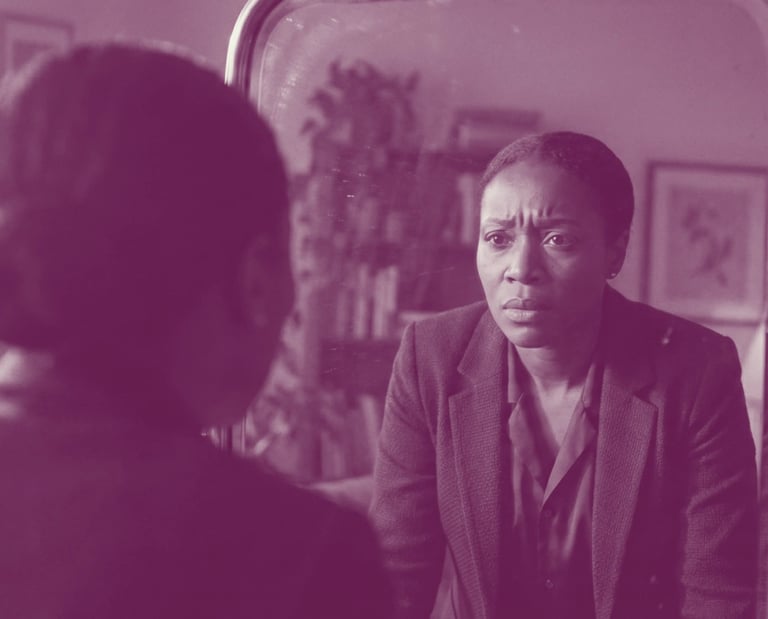 A Black woman in a blue blazer looks intensely at her reflection in an antique mirror