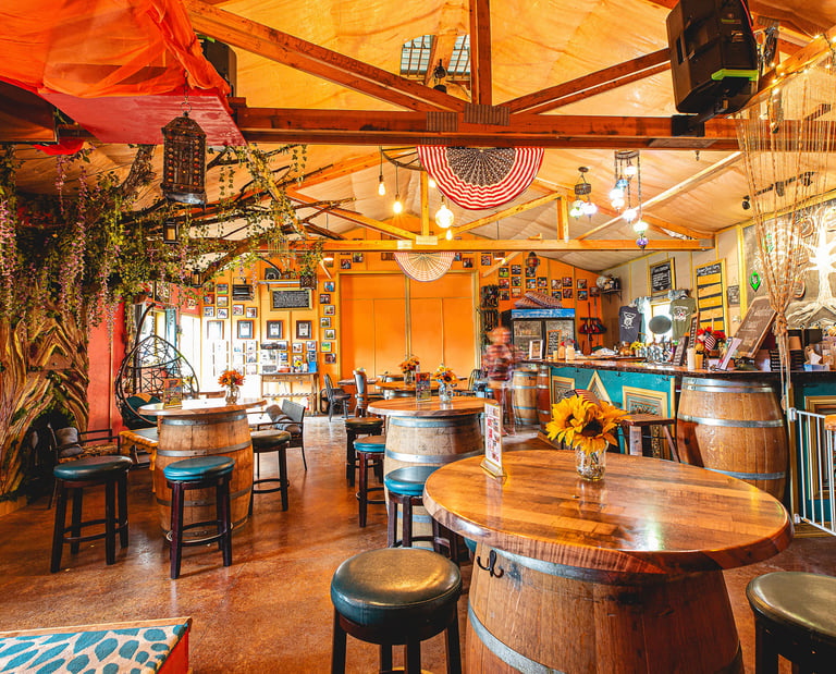 Rustic indoor pub featuring barrel tables, bar stools, and warm decorative lighting for a cozy atmosphere.