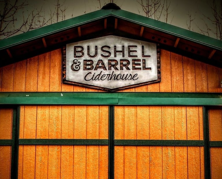 Rustic wood exterior of Bushel & Barrel Ciderhouse with a branded sign and green trim.