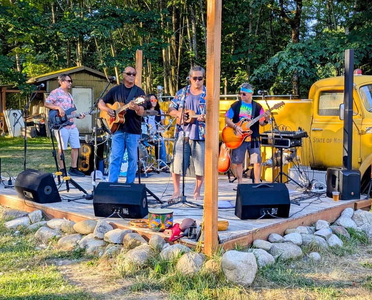 Live band performing on an outdoor stage with guitarists and a drummer at a summer music festival.