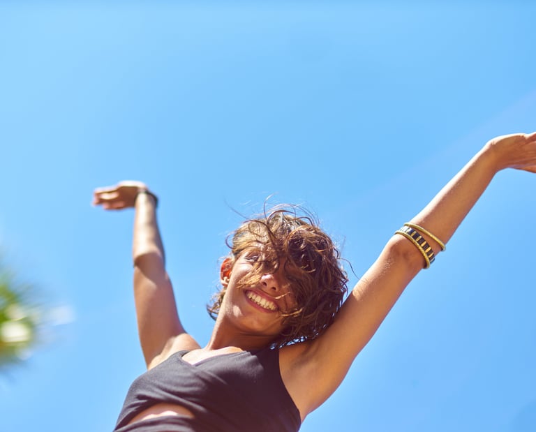 A happy woman with arms raised against a clear blue sky, expressing freedom and joy during a summer vacation.