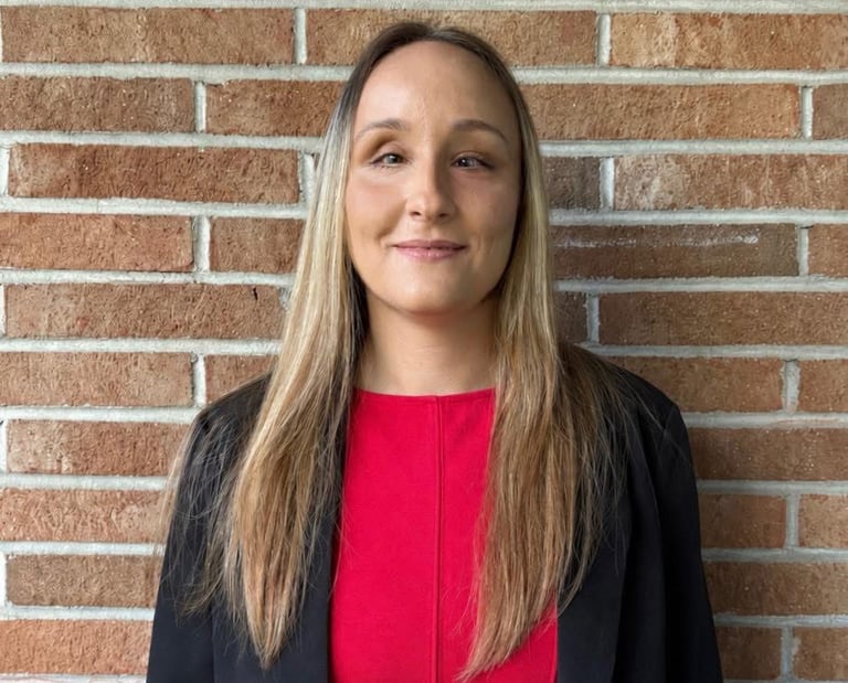 Founder Zhenya wears business attire and poses for a photo in front of a brick wall.