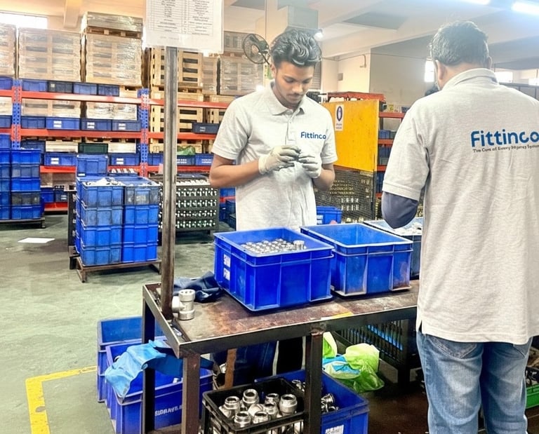 Factory workers at Fittinco inspecting high-quality hydraulic hose fittings in a manufacturing warehouse.