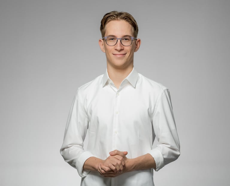 Junger Mann mit Brille in weißem Hemd lächelt freundlich vor neutralem Hintergrund