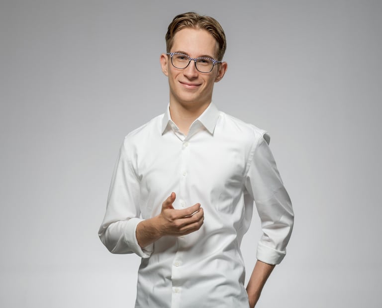 Junger Mann mit Brille in weißem Hemd lächelt freundlich vor neutralem Hintergrund
