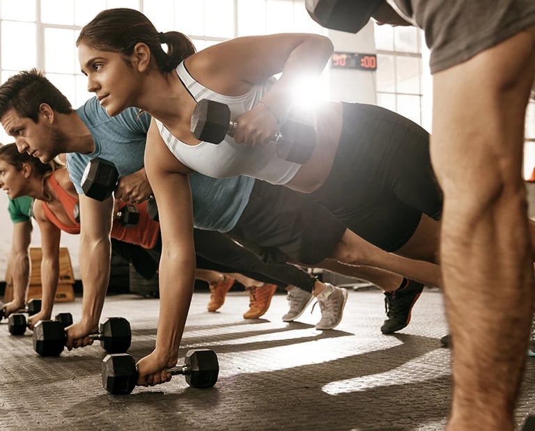 Diverse group performing renegade rows with dumbbells during a high-intensity gym workout.