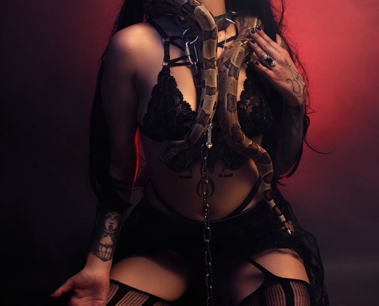 A gothic woman in black lace lingerie posing with a large boa constrictor snake in a red hazy studio.