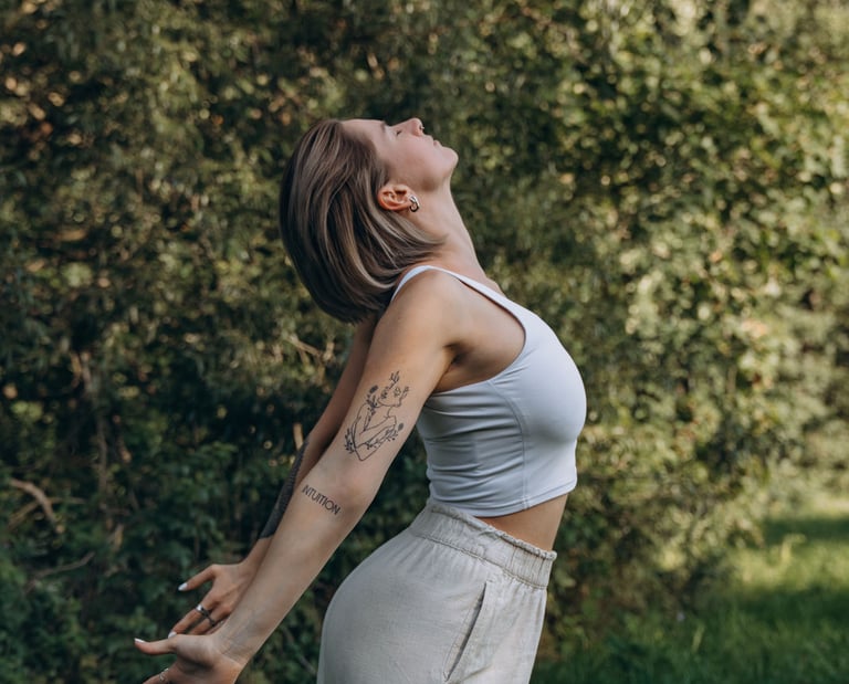 A young woman with tattoos practices mindful stretching in a lush green forest setting.