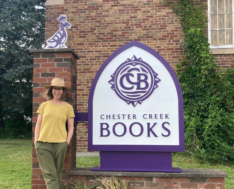 Owner Tina standing in front of purple and white Chester Creek Books sign
