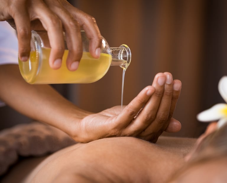 Thai aroma massage. A masseuse pores oil from into her hand above the bare back of a  lady