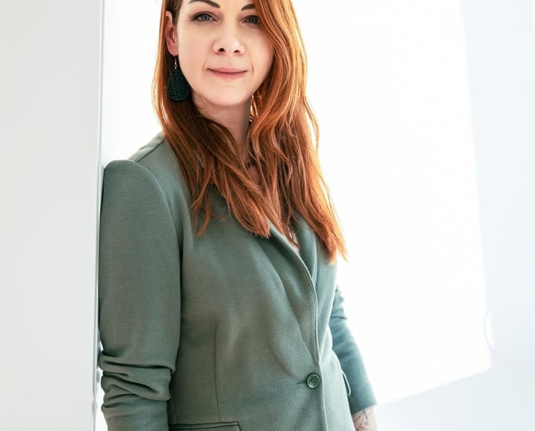Professional woman with red hair wearing a green blazer in a bright, modern office.
