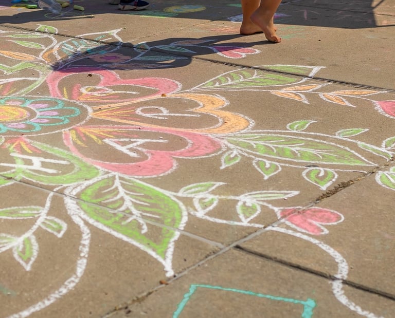 Colorful sidewalk chalk art featuring a large floral design with hearts and leaves on a concrete path.