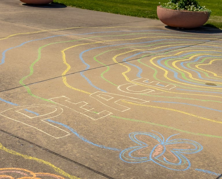 Colorful chalk art on a concrete sidewalk featuring the word PEACE and a butterfly drawing.