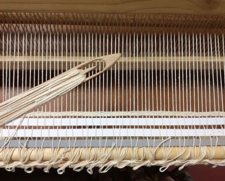 a weaving loom with a white cotton warp and a wooden shuttle with white cotton thread