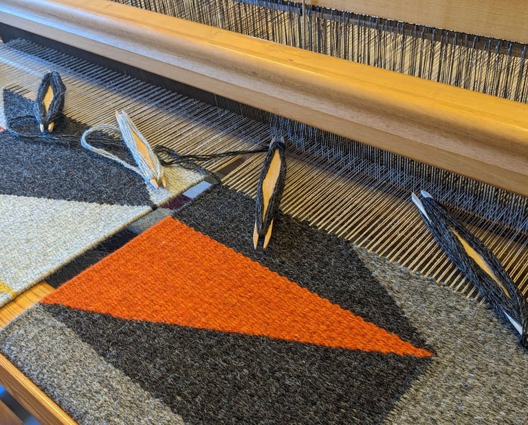 a weaving loom with shuttles and gray orange yellow black wool threads on a kilim rug in progress