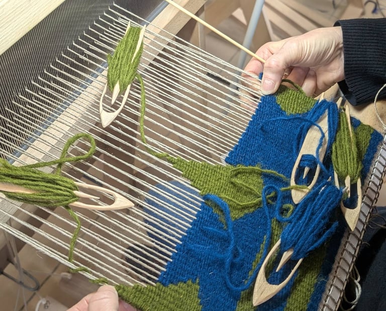 Stagiaire tissant un kilim géométrique en bleu et vert sur un métier à tisser avec navettes