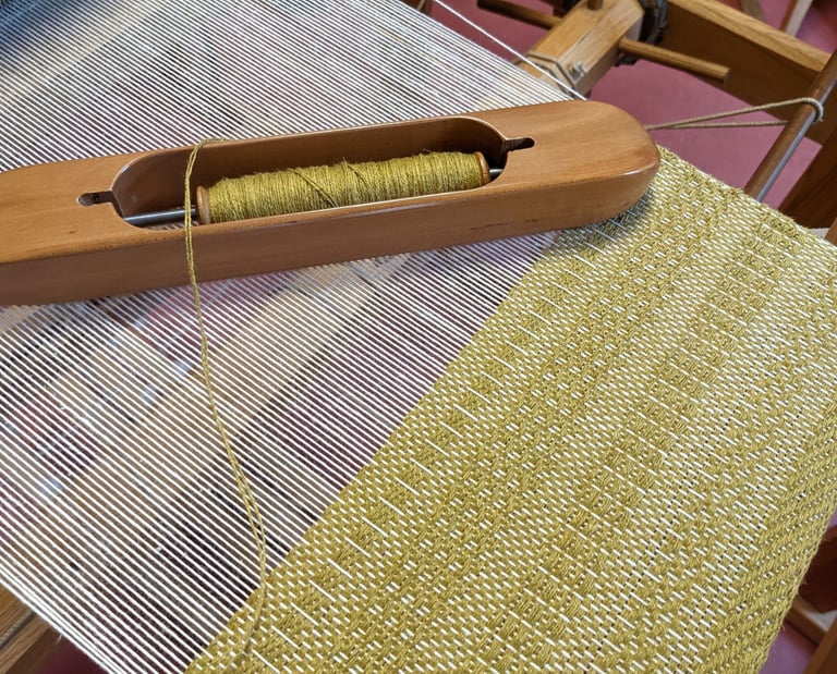 a weaving loom with shuttle and olive green threads on a 4 harness textile in progress