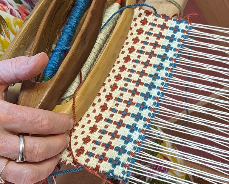 Wooden shuttles and thread spools are used to weave blue, brown, and white crosses on a weaving loom