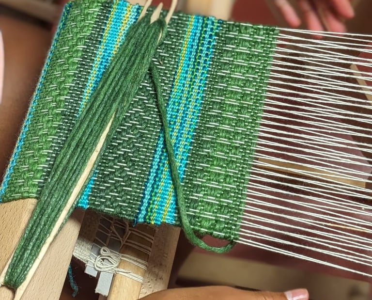 a woman working on a weaving loom with shuttle and green blue threads on a textile in progress