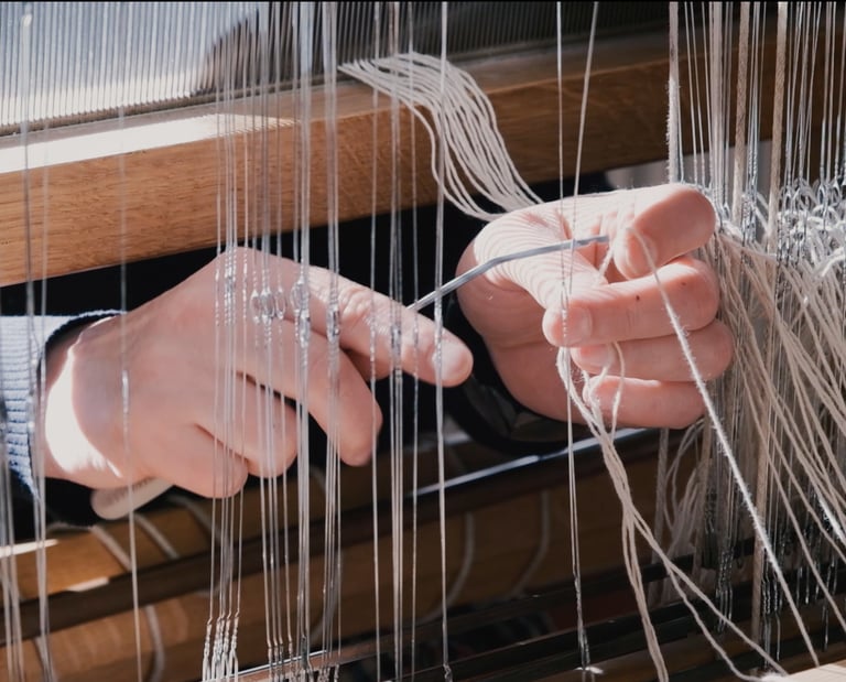 A person inserts the warp threads through metal eyelets of the harnesses