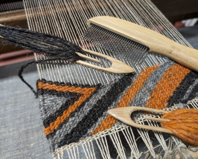a weaving loom with shuttle, combe and black grey orange wool  threads on a navajo rug in progress