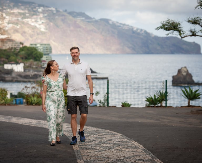 Couple walks along Funchal Lido Promenade, Madeira, with Atlantic coast and scenic cliffs in the background, lifestyle mood.