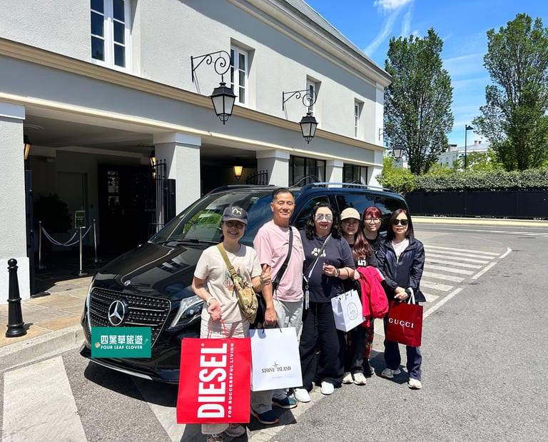 A group of tourists holding luxury brand shopping bags poses next to a black Mercedes-Benz chauffeur van.