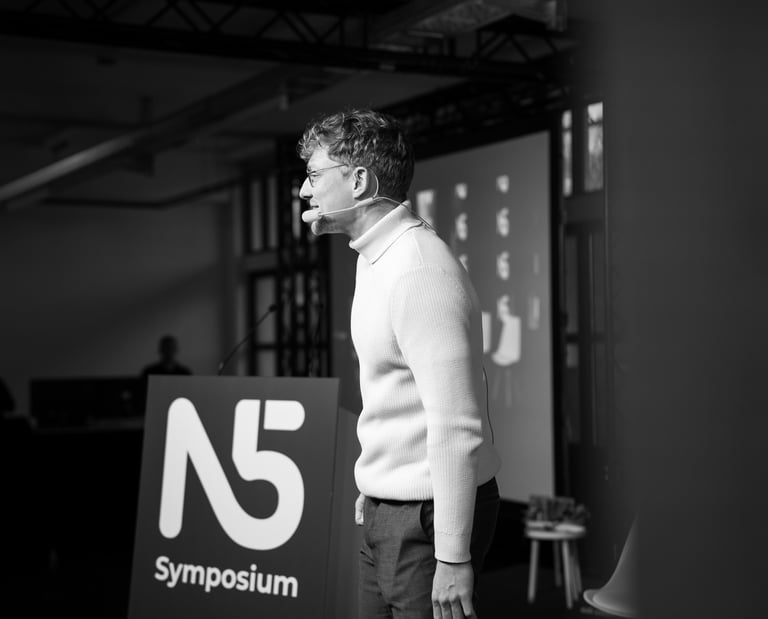 Moderator Przemek, Przemysław Żuk, steht auf einer Bühne und spricht lächelnd das Publikum an. Schwarz-weiß.