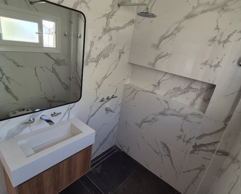 Modern bathroom featuring white marble wall tiles, a floating vanity with a wooden cabinet, and a walk-in shower.