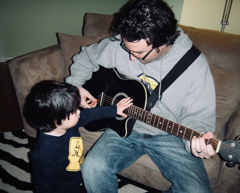 A father sitting while playing guitar with his toddler
