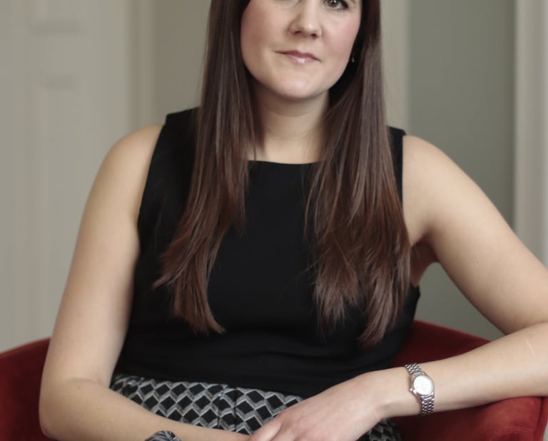 Photo of Anna Joyce, CBTI insomnia therapist in UK, sitting in red chair wearing a black dress
