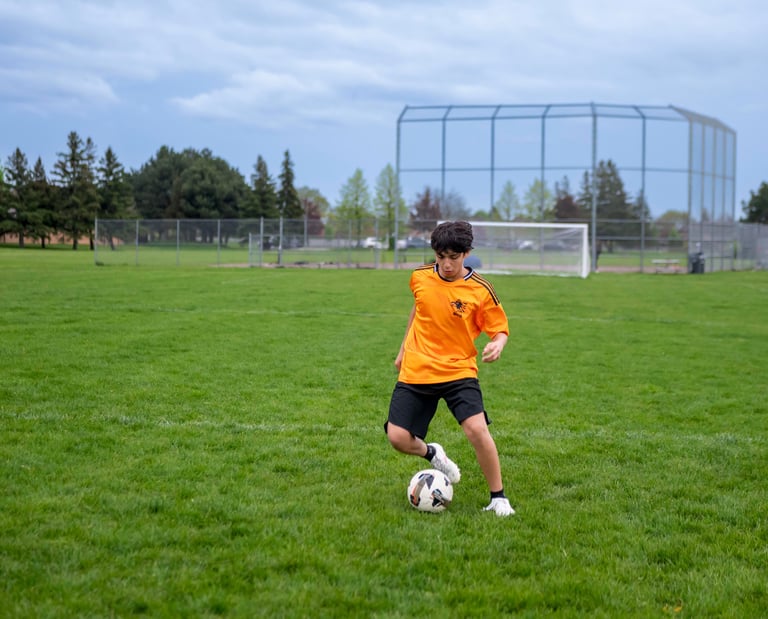 Young male soccer MVB FC student dribbling a ball on a green grass in Mississauga