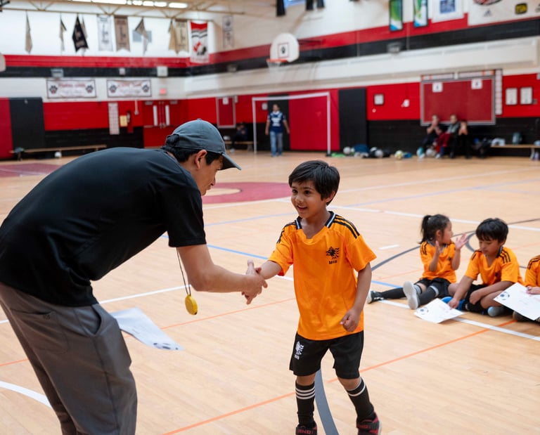 A youth indoor soccer coach shakes hands with a young player at MVB FC during Soccer class.